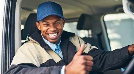 Portrait of a courier showing thumbs up while driving a delivery van.
